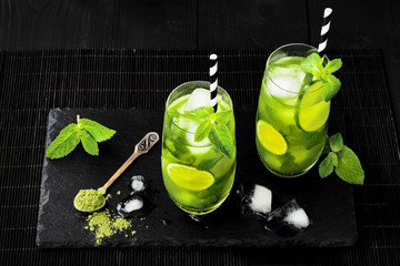 Wall Mural - Matcha iced green tea with lime and fresh mint on black stone slate background. Super food drink