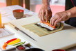 © DenisProduction.com - Man's hands touch bamboo mat. Nori leaf and raw fish. Sushi chef prepares futomaki rolls. Only fresh and quality ingredients.