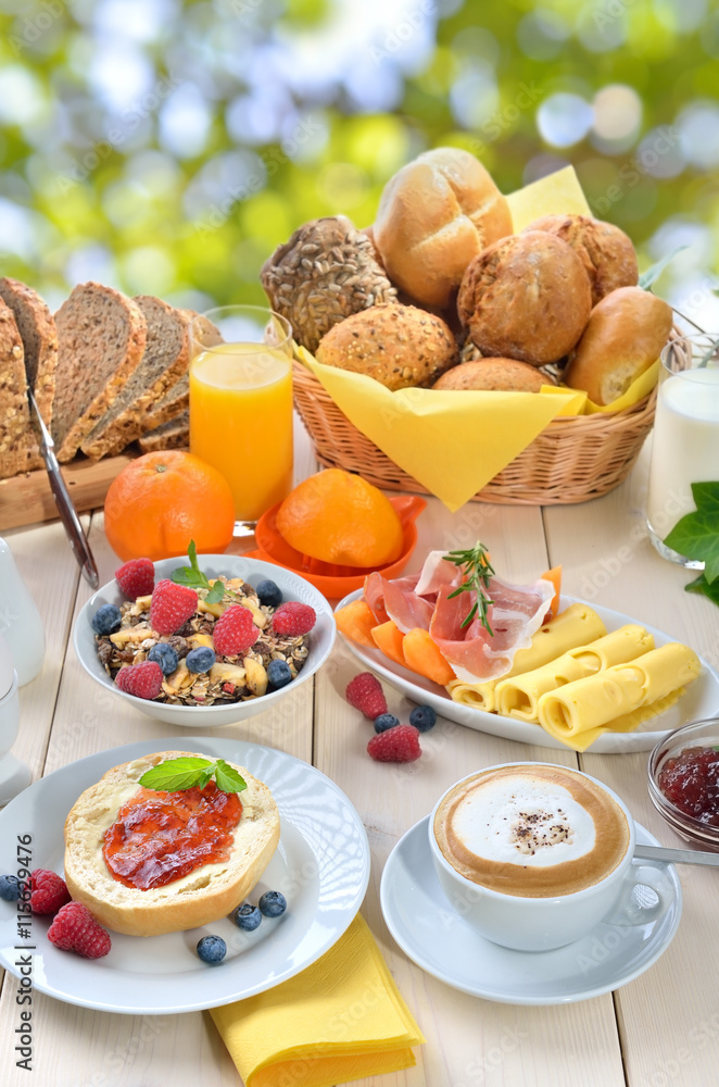 Gedeckter Frühstückstisch mit reichlicher Auswahl vor sommerlichem Laub- Outside served breakfast in summer with a cup of cappuccino and a large selection of food Stock Photo