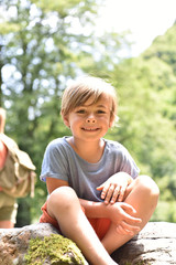 portrait of cute little boy sitting on rock by river