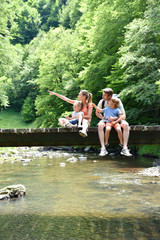 Wall Mural - Family sitting on a bridge crossing mountain river