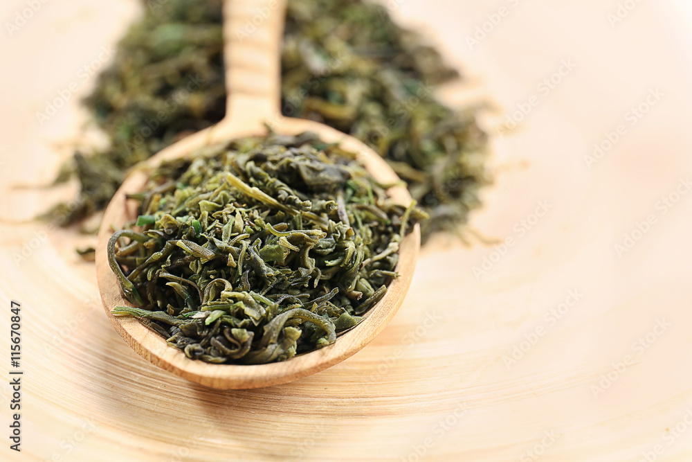 Dry tea leaves in wooden spoon on table