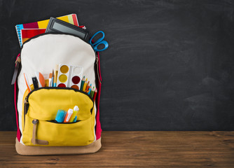 backpack full of school supplies over black school board background