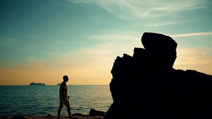 Wall Mural - Man climbs on a rock at sunset on the beach-2
