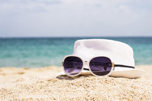 Close Up Of White Hat And Sunglasses On The Beautiful Sand Beach As Summertime Concept