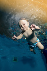 Wall Mural - Happy baby learns to swim underwater in the pool. Portrait. Bottom view. Vertical orientation