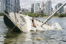 Sinking Sailboat Abandoned On The Shore Of A City
