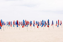 Man Standing Among Closed Parasols On Beach