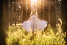 Beautiful Young Woman Wearing Elegant Light Blue Dress Standing In The Forest With Rays Of Sunlight Beaming Through The Leaves Of The Trees. Toning