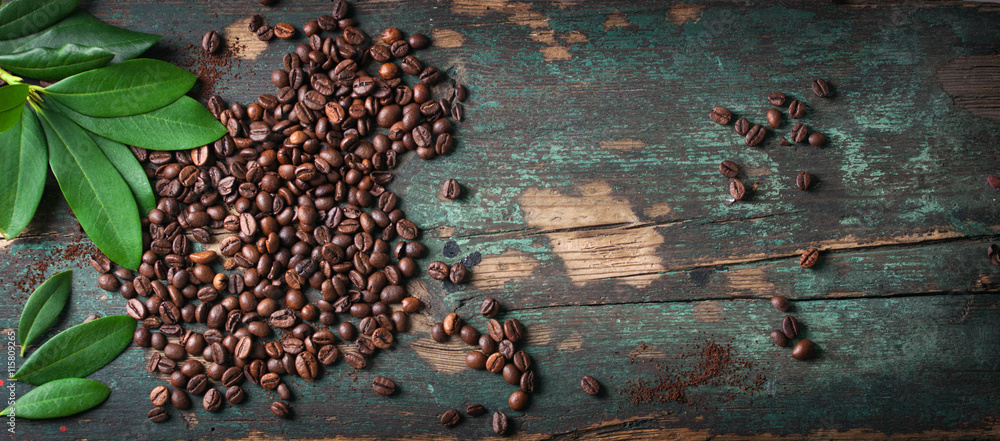 Roasted coffee beans with green leaves on a vintage background, top view with copy space - obrazy, fototapety, plakaty 