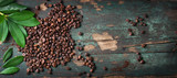 Fototapeta Kawa jest smaczna - Roasted coffee beans with green leaves on a vintage background, top view with copy space