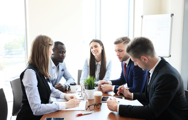 Wall Mural - Young handsome woman gesturing and discussing something while his coworkers listening to him sitting at the office table