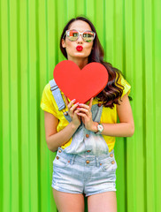 Beautiful smiling woman holding a red heart over green backgroun