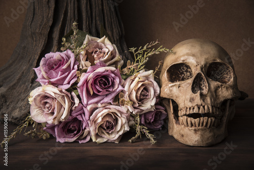 Bouquet purple roses with human skull over tree background on wooden table st...