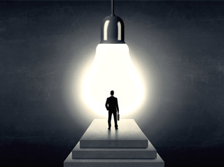 Wall Mural - Man standing on a step in front of a huge light bulb