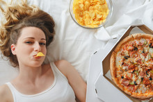 Girl Eating Chips On The Bed, Standing Next To Pizza