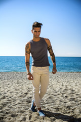 Wall Mural - Full Length Shot of a Handsome Athletic Young Man in Trendy Attire, on a Beach in a Sunny Summer Day, Looking Away against Blue Sky Background.