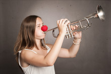 Woman With Red Nose Playing Trumpet On A Gray Background