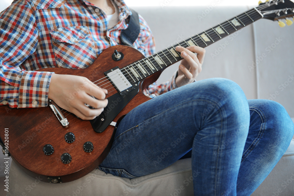 Young man playing electric guitar on grey sofa at home