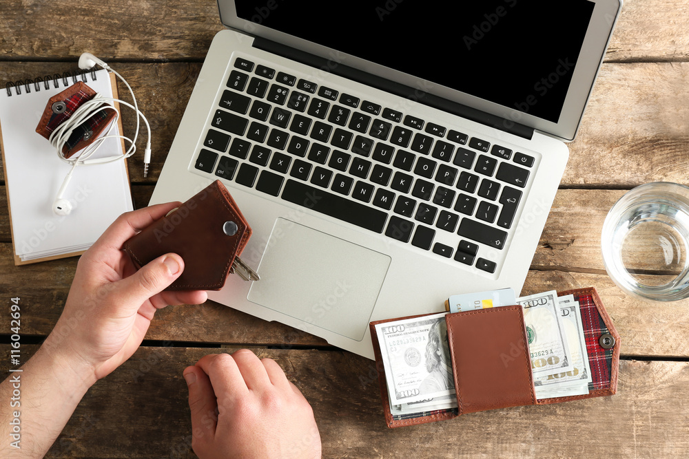 Man hands with keys, laptop and wallet on wooden table