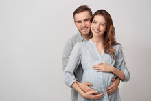 Happy Family Expecting Baby On Light Background