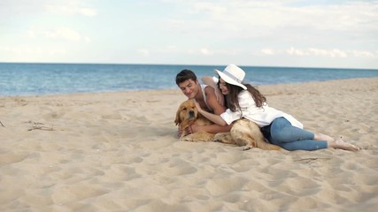 Canvas Print - Young beautiful couple in love sitting on the beach playing with dog