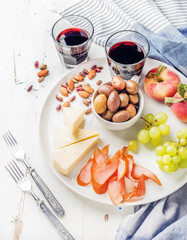 Wine snack set. Cheese, chicken carpaccio, mediterranean olives, fruits, nuts and two glasses of red on ceramic plate over white wooden background