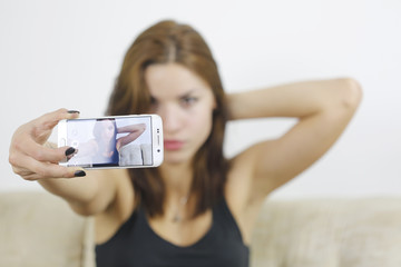 Beautiful young woman photographing herself with phone at home