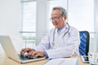 © DragonImages - General practitioner working on laptop at his table