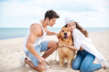 Couple sitting and hugging their dog on the beach