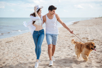 Wall Mural - Young couple running along the beach with their dog