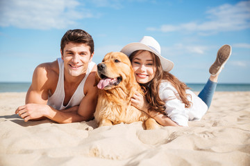 Wall Mural - Happy young couple hugging with dog on the beach