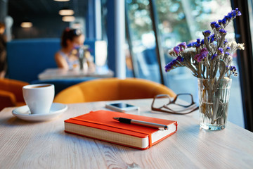 free table with cup, notebook and eyeglasses at a table made of wood . in the background a bright window with bright daylight. business or education concept