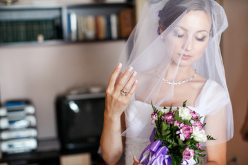 Pretty bride looks at a wedding bouquet adjusting her veil