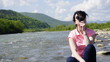 © andrii kobryn - Portrait of smiling beautiful young woman with round glasses sitting on the stone and making funny faces. Carpathian mountain river background