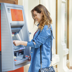 Happy brunette woman withdrawing money from credit card at ATM