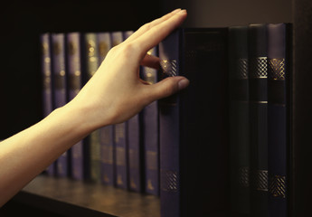 Wall Mural - Books in a row on a bookshelf. Hand taking a book