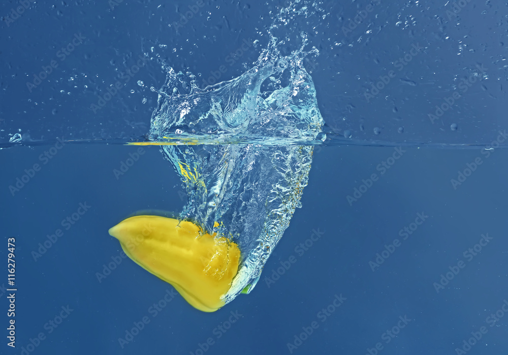 Fresh yellow pepper falling in water on dark background