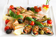 Close-up of plate with assorted cooked seafood and spicy sauce on white wooden background. Marine cuisine