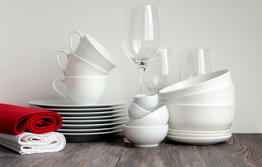 Wall Mural - White dishware stacked on a wooden table against black background with transparent wineglasses and rolled layovers