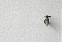 Old Faucet Next To A White Wall.