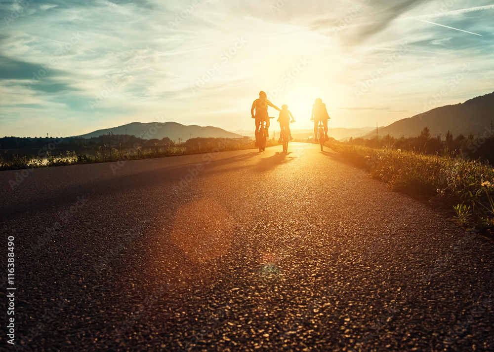 Ð¡yclists family traveling on the road at sunset - obrazy, fototapety, plakaty 