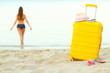 © vladstar - Yellow suitcase on the beach and a girl walks into the sea in th