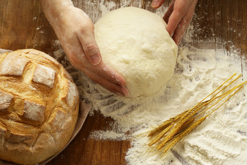 Chef hands with dough and homemade natural organic bread and flour on a wooden background