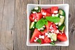 Summer salad with watermelon, cucumber and feta cheese in a square bowl, above view on wood background