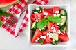 Delicious watermelon, cucumber and feta cheese salad in square bowl, overhead scene on marble