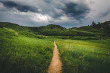 Landscape Of A Trail Leading Into Field With Hills Before A Storm.