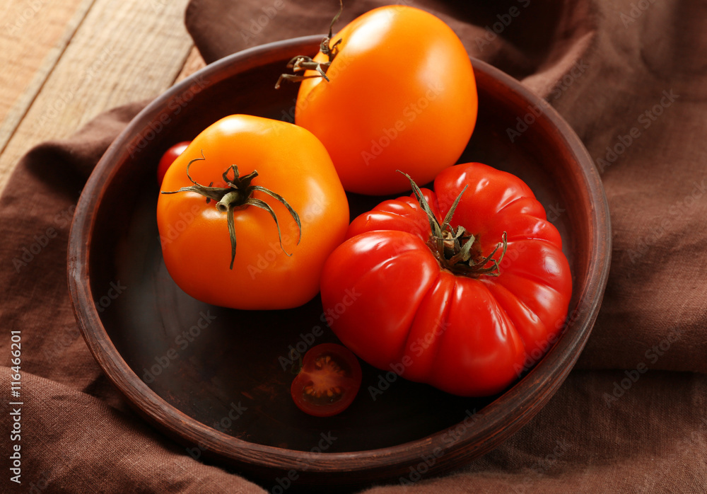 Juicy tomatoes in wooden plate on brown tablecloth