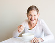 © Natalie Board - Older woman with short hair and white top laughing and eating soup from a white bowl