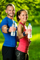 Man and woman drinking water from bottle after fitness sport exercise. Smiling couple with bottles of cold drink outdoors